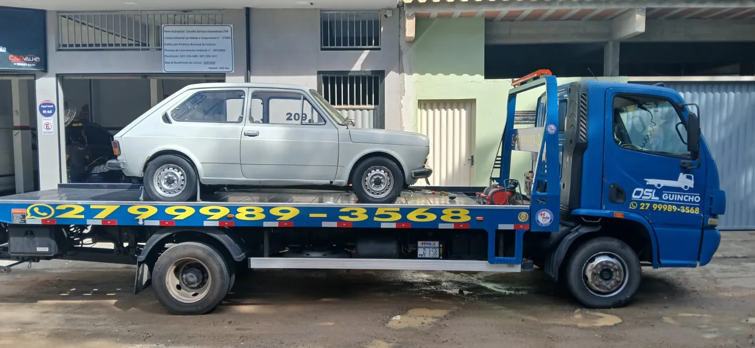 Caminhão plataforma azul da OSL Guincho transportando um Fiat 147 antigo